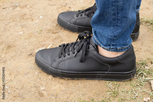 Men's feet in black sneakers and jeans stands on the ground in Ukraine, men's feet and shoes