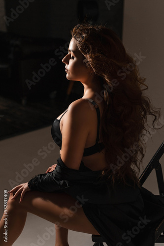 a girl with a magnificent hairstyle with curls and a make-up in a black erotic robe and underwear in a studio on a white background on a cyclorama © Alina Belych