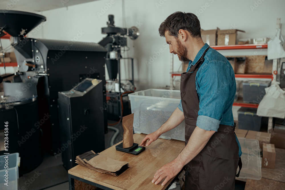 Man barista weighs paper bag with coffee beans on a scale at a coffee factory Man barista weighs paper bag with coffee beans on a scale at a coffee factory