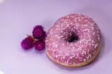 Donut and purple Icing And Colored Sprinkles on purple background and dry violet flower. Tasty delicious fat high calories sweet food. Selective Focus. Birthday donut treat doughnut - isolated dessert