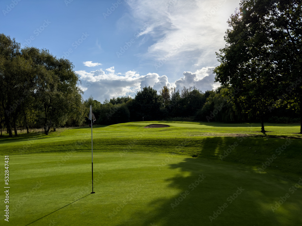 Obraz premium Flag and the hole at golf club blue sky summers day with some clouds