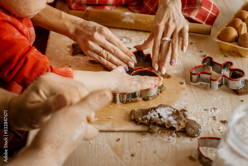 Side close up view of family member's hands cutting out different Christmas shapes out of raw dough to bake festive Christmas gingerbread cookies