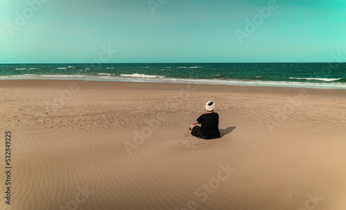 Mature woman in turban resting on lonely beach. Copy space.