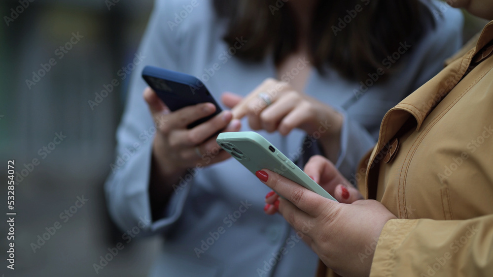 Close up focus on females hands using phones. Two women with smartphones on the street, the girl explains, shows, tells, demonstrates, gesticulates with her hand