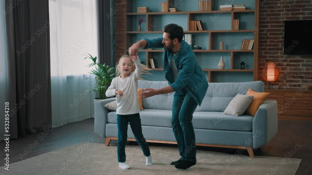 Happy millennial daddy dancing with little beautiful artistic daughter teach child dance active preschool girl kid holding father hands twist jumping to music together in living room funny home party Happy millennial daddy dancing with little beautiful artistic daughter teach child dance active preschool girl kid holding father hands twist jumping to music together in living room funny home party