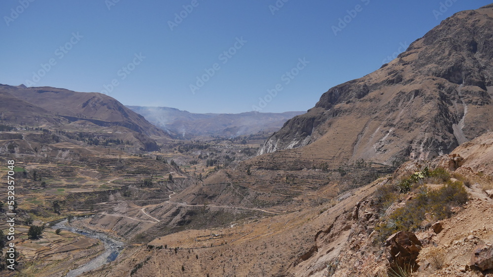 Une route passant à travers de hautes montagnes, avec des champs d'agriculture en bas, traversée péruvienne, en plein jour, terre sec et rouge, orange