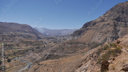 Une route passant à travers de hautes montagnes, avec des champs d'agriculture en bas, traversée péruvienne, en plein jour, terre sec et rouge, orange © Nicolas Vignot