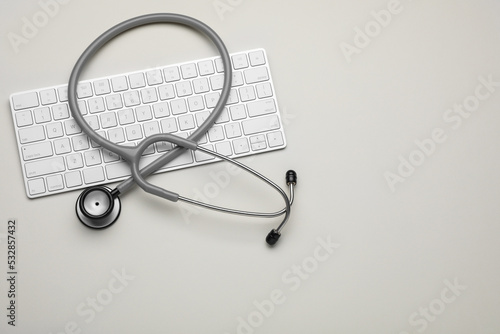 Keyboard and stethoscope on beige background, flat lay. Space for text