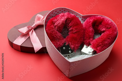 Gift box with furry handcuffs on red background