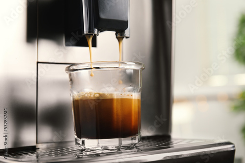 Espresso machine pouring coffee into glass against blurred background, closeup. Space for text