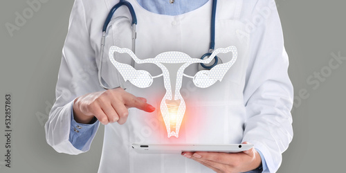 Doctor holding modern tablet and virtual image of uterus on grey background, closeup photo