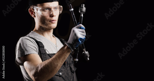 steering rods in the hand of an auto mechanic, craftsman on a dark background. Car steering repair concept.