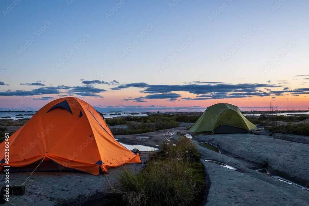 Tents set up on the smooth rock of Georgian Bay seen as the sunset turns clouds pink and blue over the water in the background.  Room for text.