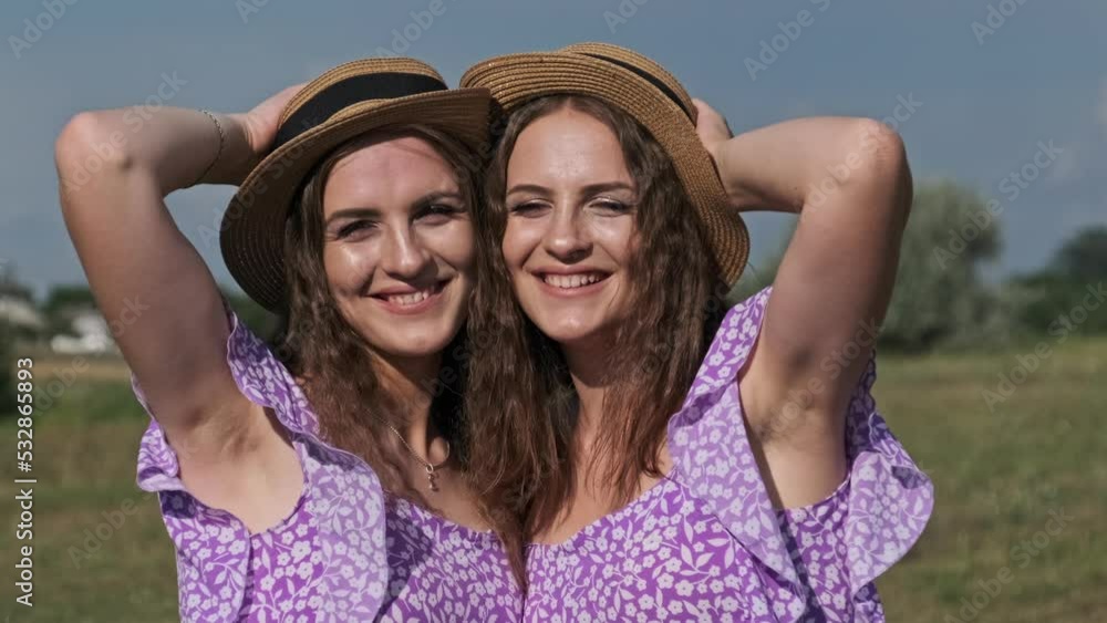 Portrait of two young twin girls in identical summer dresses and straw