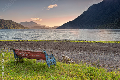 Bench on the beach near the town of Hornopiren with a peaceful view on the Comau fjord at sunset. The Comau fjord, also known as Leptepu, penetrates the mainland of Chile, in Los Lagos Region. photo