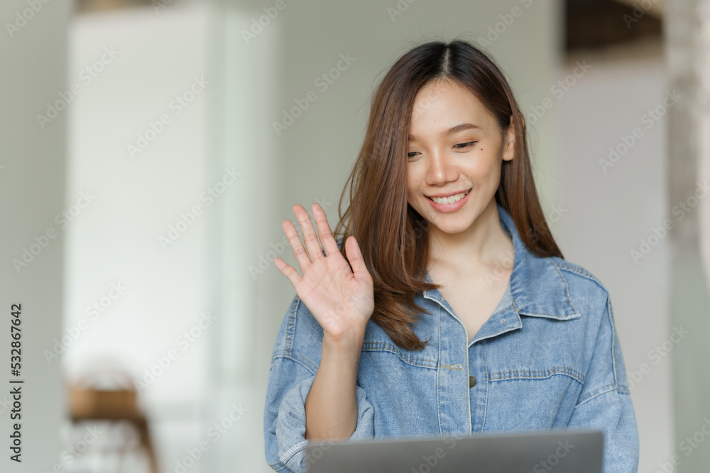 Young happy pretty asian woman using laptop at cafe, hand wave, say hi, hello.