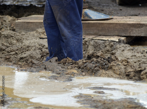 The lower legs of a worker on a muddy site during maintenance and construction.