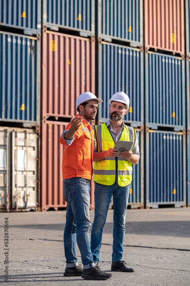 Logistics engineer and inspector working togetter and discussing with Shipping container stacker background in commercial transport port
