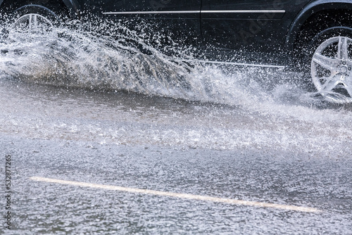car splashes through a large puddle on a wet road. driving in heavy rain.