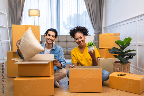 Young couple unpacking cardboard boxes at living room.Moving house. happy smiling woman unpacking boxes sitting near sofa at new home. © anon