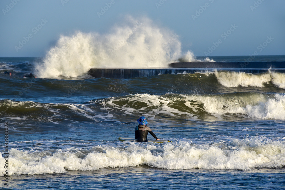 Naklejka premium Female surfer looking at dangerous waves by pier