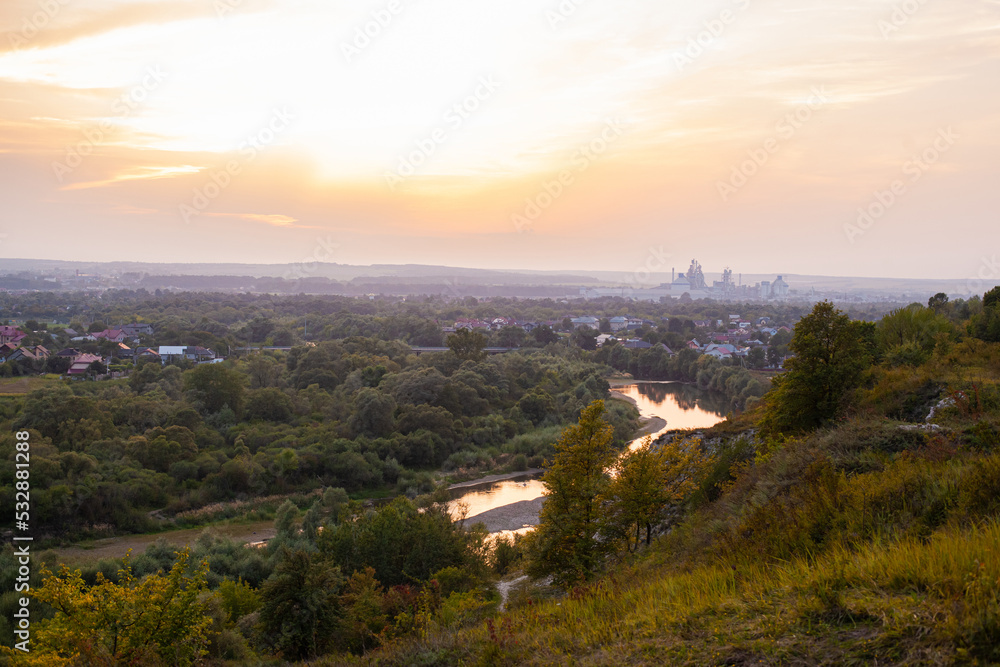 Fototapeta premium Panoramic view of the city of Ivano-Frankivsk. View of mountain hill and industrial power station oland behind at evening. Sunset over Ivano Frankivsk city in Ukraine. Landscape with hills and river.