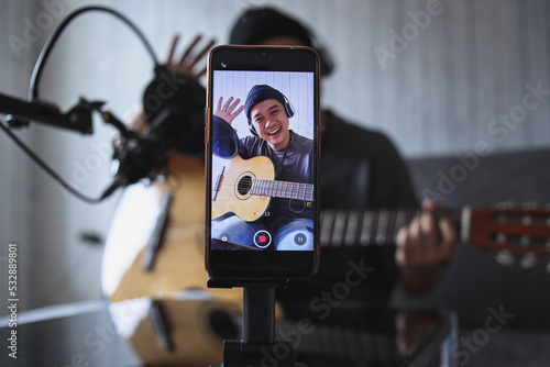 Asian influencer playing guitar during podcast or live video broadcast for the audience from the mobile phone at home photo