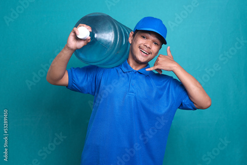 Asian delivery guy in blue uniform work as dealer courier, holding water bottle while doing phone gesture