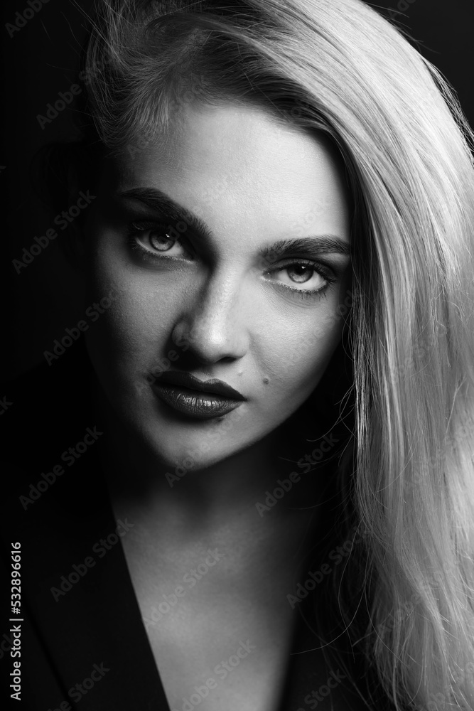 Fashion, make-up and business concept. Black and white studio portrait of beautiful woman with long bright hair looking at camera with seductive look. Model wearing classic black suit