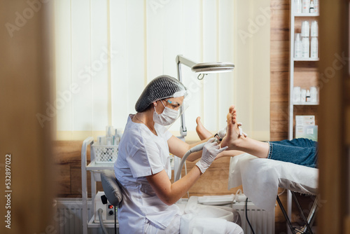 Podologist foot doctor in mask on face, making procedure for foot with special equipment