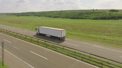 Aerial shot of a fast truck on the road in beautiful countryside with green grass in the summer