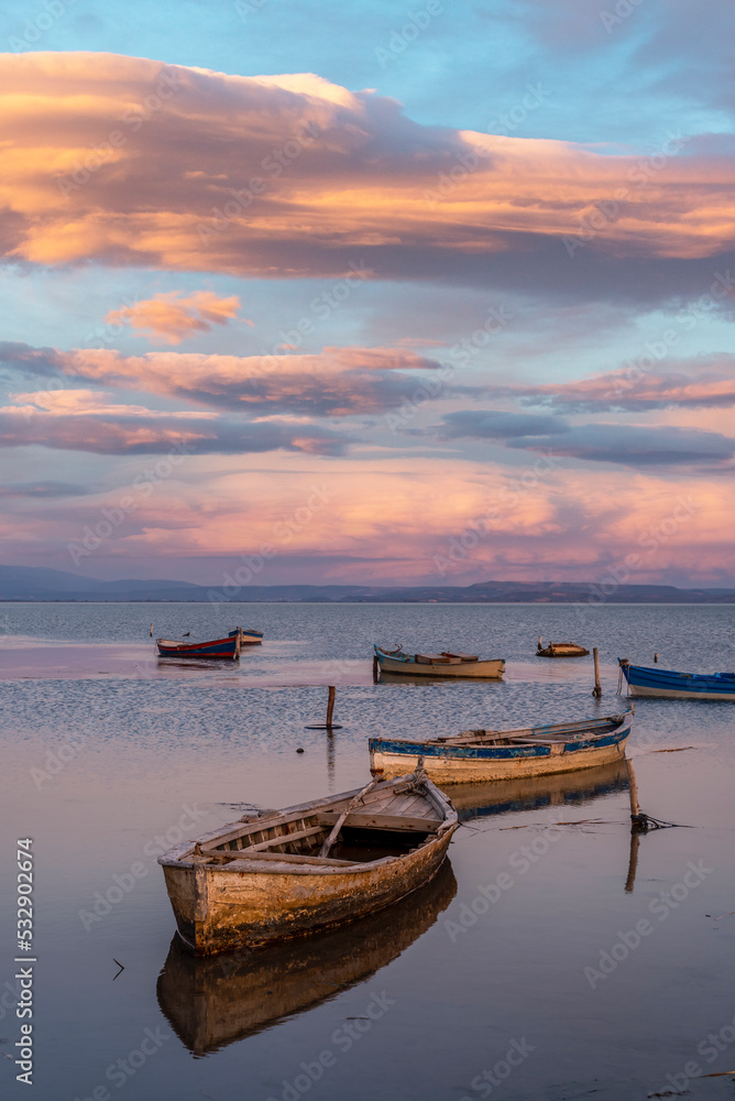 Boats on water, colorful sky and clouds with reflection on water and fishing boats on the sea