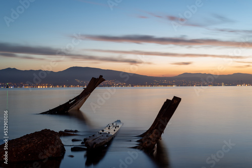 Long exposure photography  sunken boat on blue sea with a city view on background moving clouds blurry concept