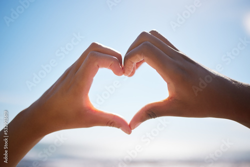 Heart sign, beach hands and blue sky on vacation by the sea, happy on international holiday in Miami and love for summer travel in nature. Person with emoji for happiness by the ocean in spring