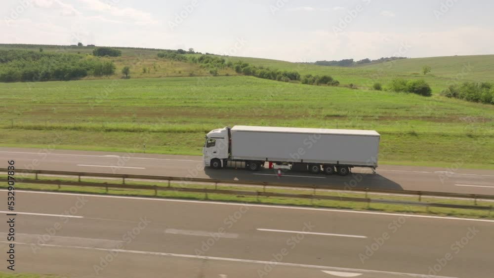 Cargo truck driving along the highway past a green field. Cloudy sky in the background Cargo truck driving along the highway past a green field. Cloudy sky in the background