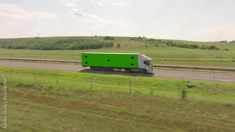 Truck with green screen passes over highway road in countryside, aerial view. Truck with semi-trailer which chromakey, rides freeway Truck with green screen passes over highway road in countryside, aerial view. Truck with semi-trailer which chromakey, rides freeway