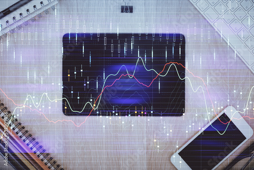 Double exposure of forex graph hologram over desktop with phone. Top view. Mobile trade platform concept.