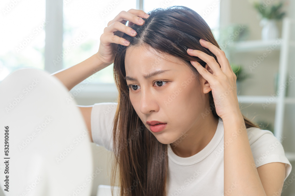 Damaged hair, face serious asian young woman, girl worry looking at scalp in mirror, hand in break into front hair loss, thin problem symptom from shampoo at home. Health care of beauty concept. Damaged hair, face serious asian young woman, girl worry looking at scalp in mirror, hand in break into front hair loss, thin problem symptom from shampoo at home. Health care of beauty concept.