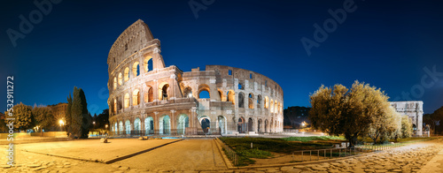 Rome, Italy. Colosseum Also Known As Flavian Amphitheatre In Evening Or Night Time. Panoramic View