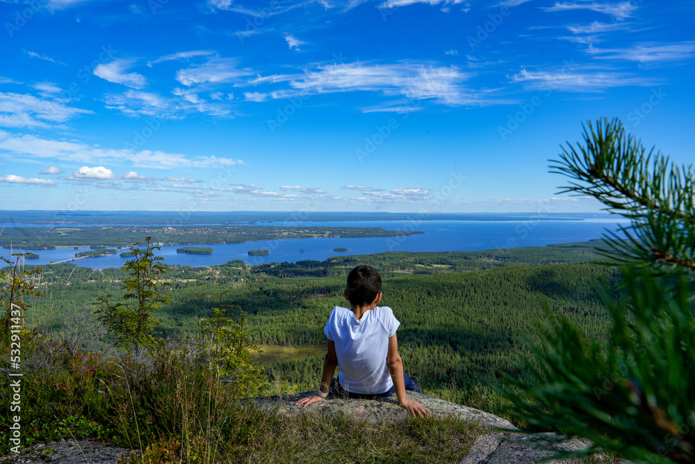 Kind schaut auf dem Berg in die Natur mit Seenlandschaft in Schweden  Skandinavien mit blauem Himmel im Hintergrund und viel Wasser