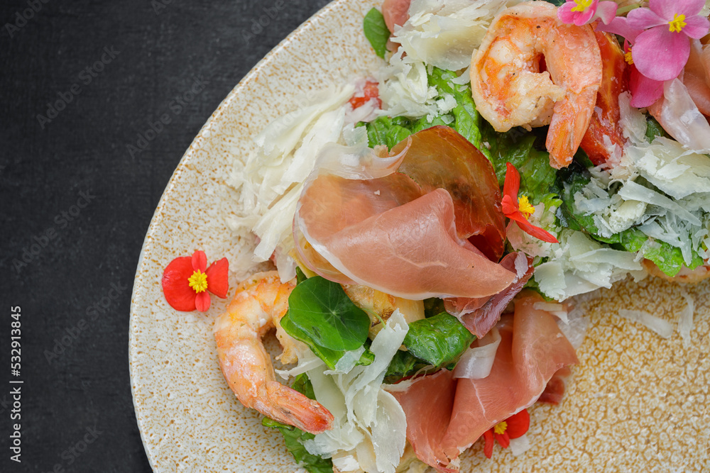 Salad with shrimps, cheese and prosciutto, on a plate