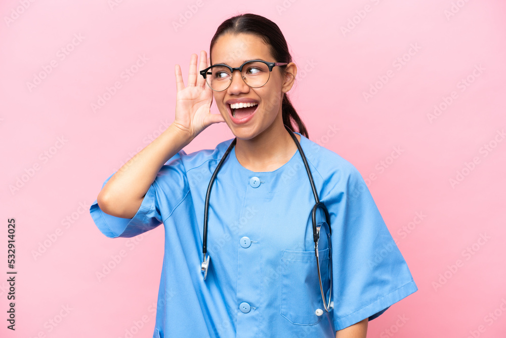 Young nurse Colombian woman isolated on pink background listening to something by putting hand on the ear Young nurse Colombian woman isolated on pink background listening to something by putting hand on the ear