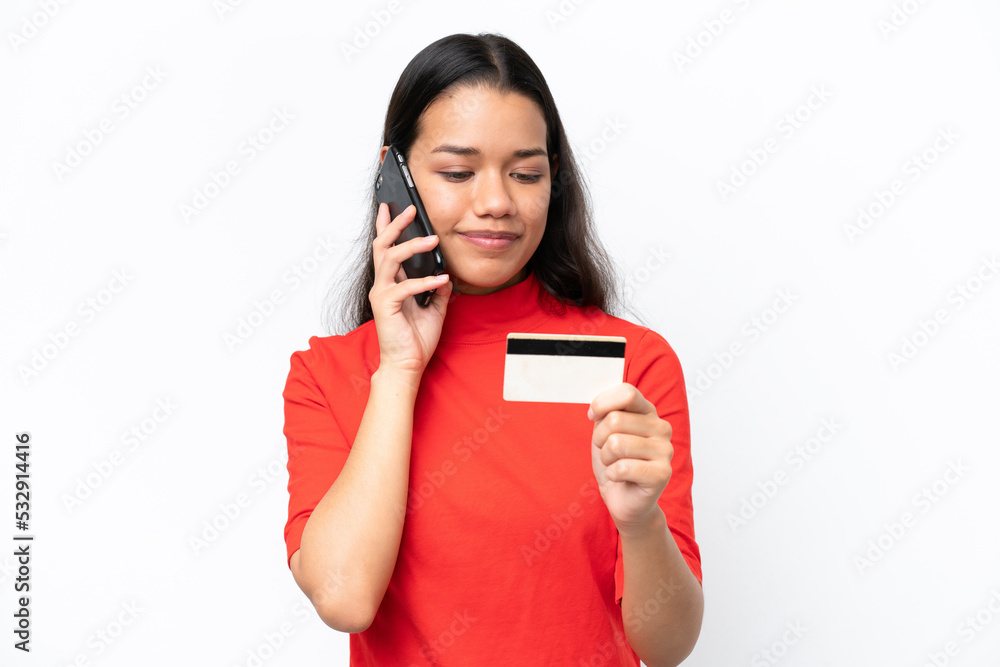 Young Colombian woman isolated on white background buying with the mobile with a credit card Young Colombian woman isolated on white background buying with the mobile with a credit card