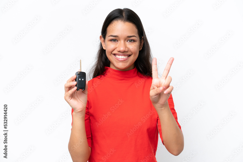 Young Colombian woman holding car keys isolated on white background smiling and showing victory sign Young Colombian woman holding car keys isolated on white background smiling and showing victory sign