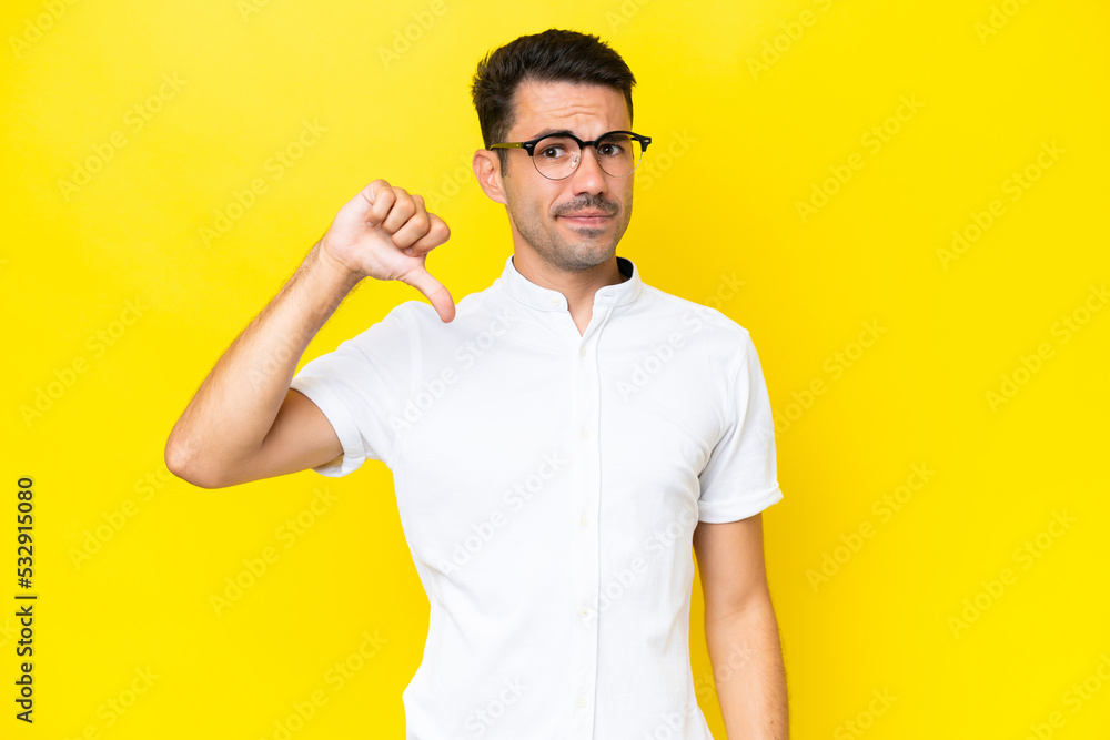 Young handsome man over isolated yellow background showing thumb down with negative expression Young handsome man over isolated yellow background showing thumb down with negative expression