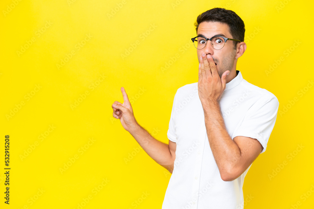Young handsome man over isolated yellow background with surprise expression while pointing side Young handsome man over isolated yellow background with surprise expression while pointing side
