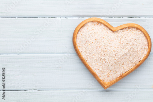 Wheat flour in a wooden heart shape bowl on a pastel background.