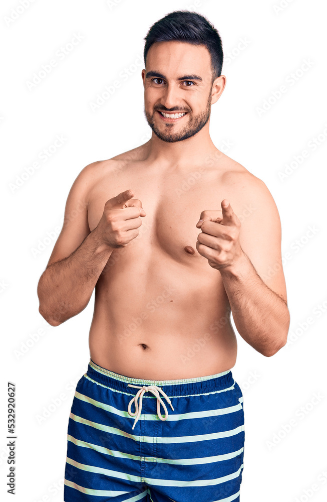 Young handsome man wearing swimwear pointing fingers to camera with happy and funny face. good energy and vibes. Young handsome man wearing swimwear pointing fingers to camera with happy and funny face. good energy and vibes.