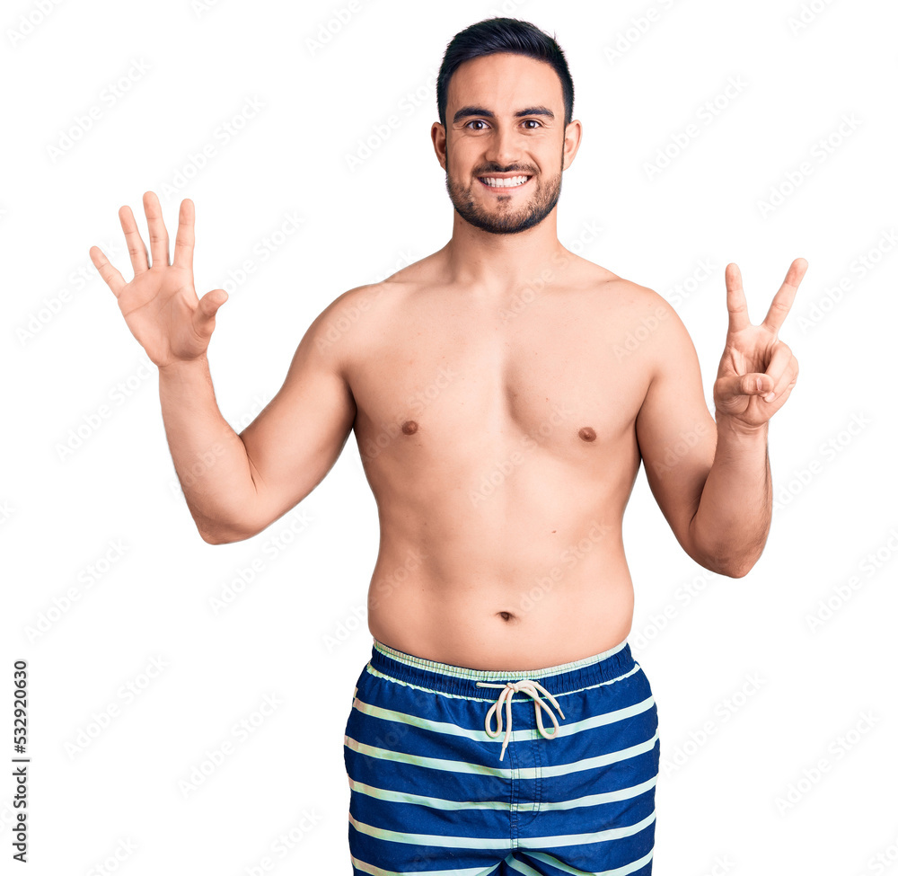 Young handsome man wearing swimwear showing and pointing up with fingers number seven while smiling confident and happy. Young handsome man wearing swimwear showing and pointing up with fingers number seven while smiling confident and happy.