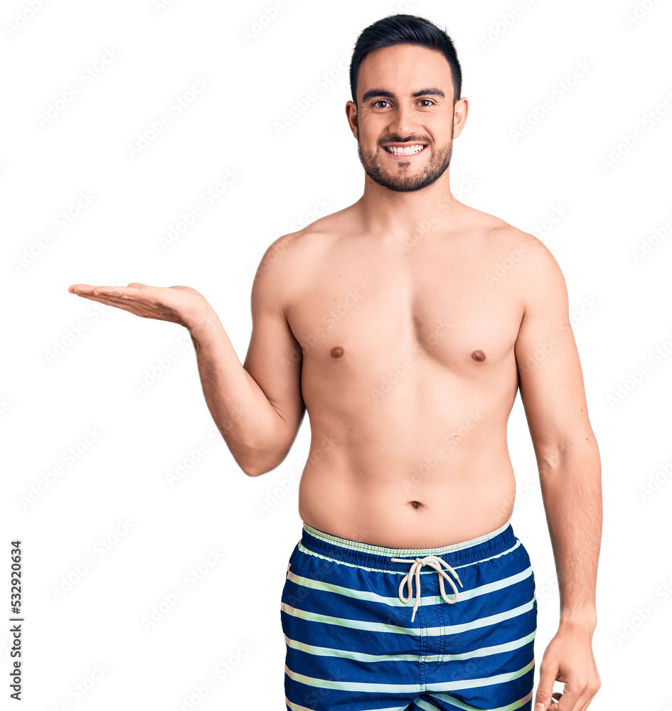 Young handsome man wearing swimwear smiling cheerful presenting and pointing with palm of hand looking at the camera. Young handsome man wearing swimwear smiling cheerful presenting and pointing with palm of hand looking at the camera.